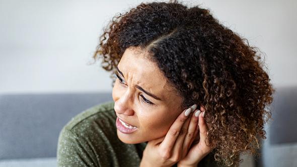 Frau mit Ohrenschmerzen hält sich das Ohr - Foto: iStock/vitapix