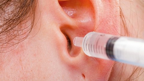 Spritze mit Flüssigkeit wird ins Ohr gehalten - Foto: iStock/Obencem