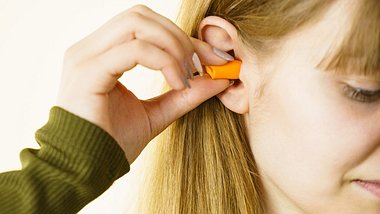 Frau platziert Ohrstöpsel im Ohr - Foto: iStock/Anetlanda