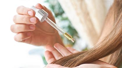 Eine Frau tröpfelt Olivenöl mit einer Pipette auf ihre Haare - Foto: iStock/Elena Volf