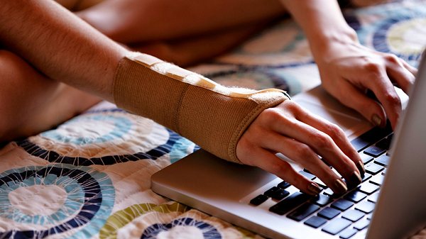 Frau mit Orthese am Handgelenk am PC - Foto: iStock/apomares