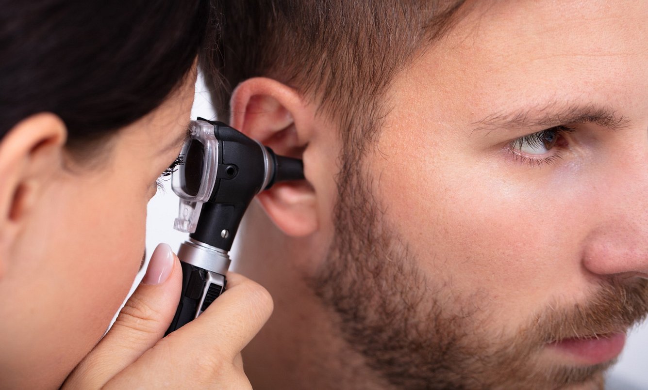 HNO-Ärztin schaut mit einem Otoskop bei einem Mann ins Ohr