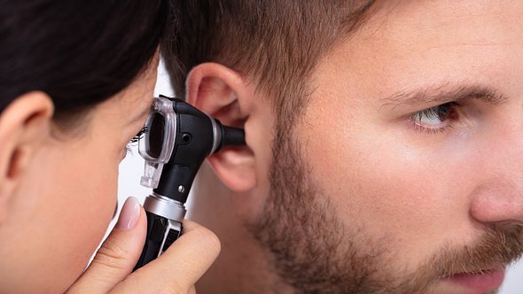 HNO-Ärztin schaut mit einem Otoskop bei einem Mann ins Ohr - Foto: iStock/AndreyPopov