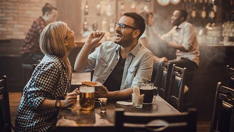 Ein Pärchen sitzt in einer Bar und isst verspielt Nüsse - Foto: iStock/skynesher