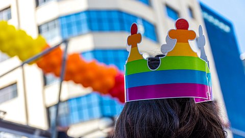Person mit einer bunten Krone auf dem Kopf schaut ein Hochhaus an - Foto: iStock/Luciano_Marques