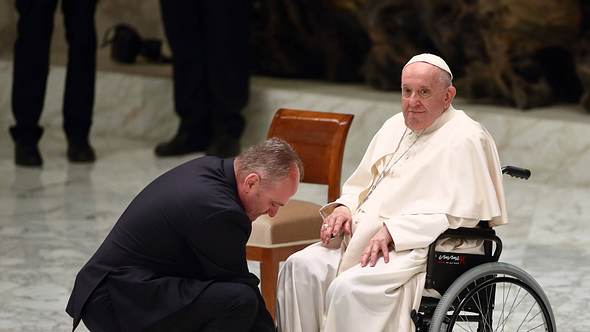 Papst im Rollstuhl, davor ein Helfer im Anzug - Foto: IMAGO/ZUMA Wire﻿﻿﻿