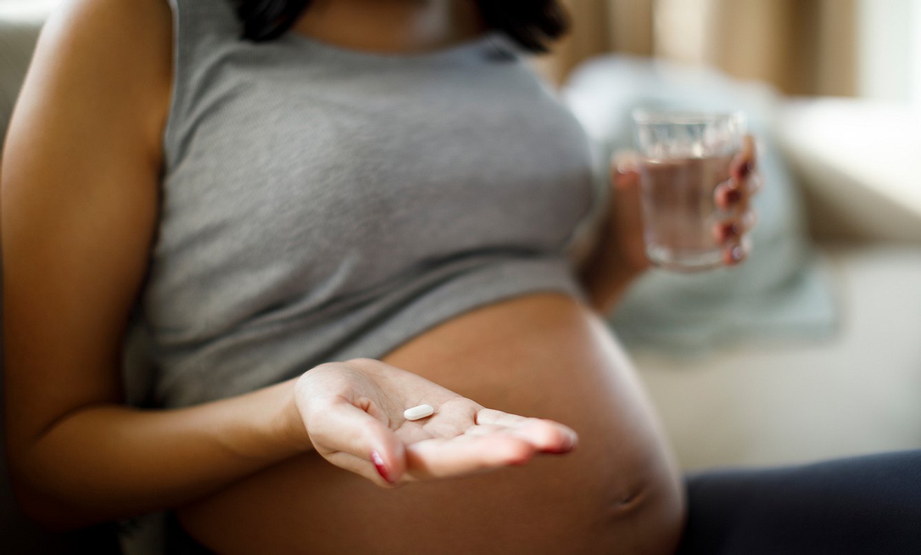 Schwangere Frau mit Wasserglas und Tablette in der Hand