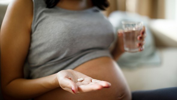 Schwangere Frau mit Wasserglas und Tablette in der Hand - Foto: iStock/damircudic