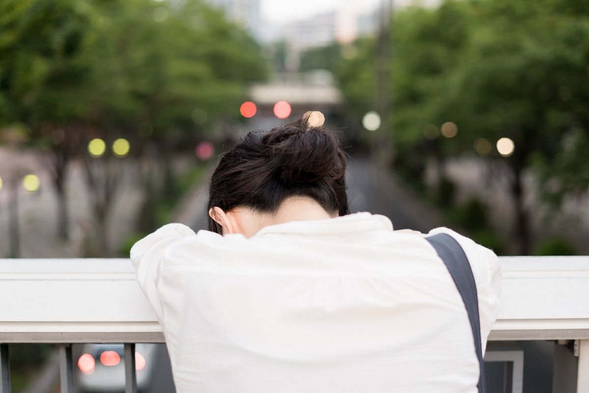 Überforderte Japanerin in einer Stadt lehnt sich erschöpft über ein Brückengeländer