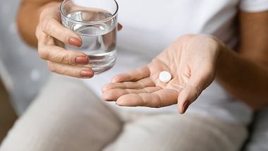 Eine Frau hält eine Tablette und ein Glas Wasser in den Händen - Foto: iStock/fizkes