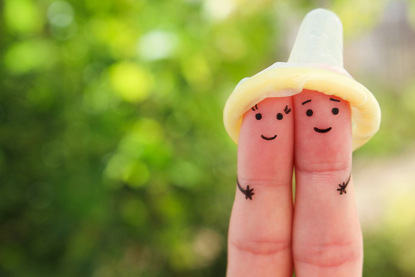 Zwei angemalte Finger mit Gesicht unter einem Kondom