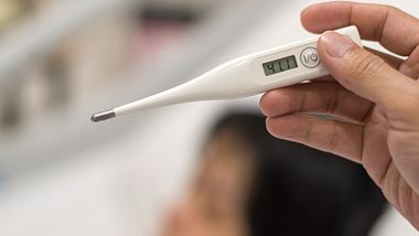 Person zeigt Fieberthermometer mit hoher Temperatur - Foto: Istock/Pornpak Khunatorn