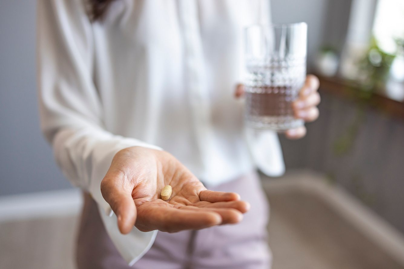 Eine Frau hält ein Glas Wasser in der einen Hand und eine Tablette in der anderen
