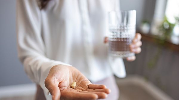 Eine Frau hält ein Glas Wasser in der einen Hand und eine Tablette in der anderen - Foto: iStock_dragana991