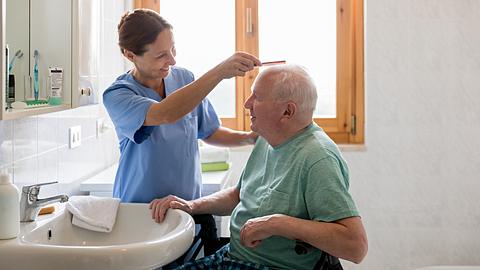 Pflegekraft mir älterem Mann im Badezimmer beim Haarekämmen - Foto: iStock/Fred Froese