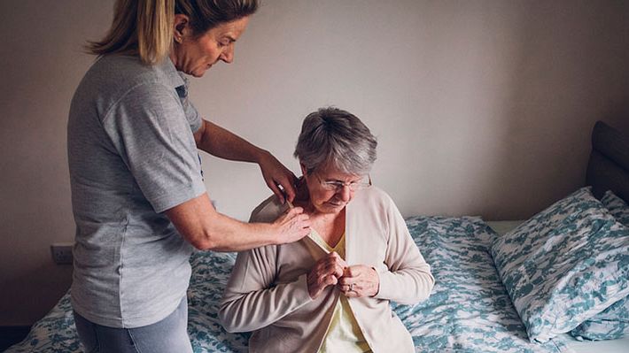 Eine Pflegehilfe hilft einer Senioren mit Pflegegrad 2 beim Anziehen - Foto: iStock/Solstock
