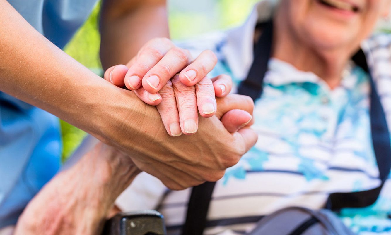 Pflegekraft hält die Hand einer alten Dame