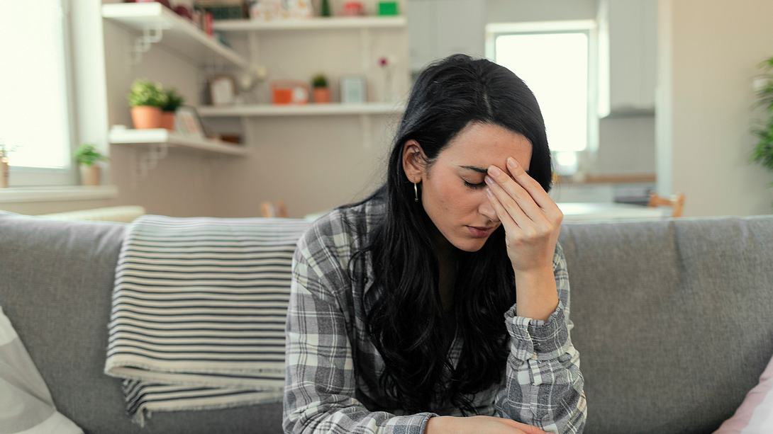 Eine Frau sitzt mit phobischen Schwankschwindel auf einem Sofa - Foto: istock_PixelsEffect