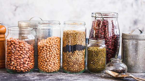 Verschiedene Hülsenfrüchte in Gläsern + Pfeffermühle, Löffel und Dose auf einem Tisch - Foto: iStock-601110870 casanisaphoto