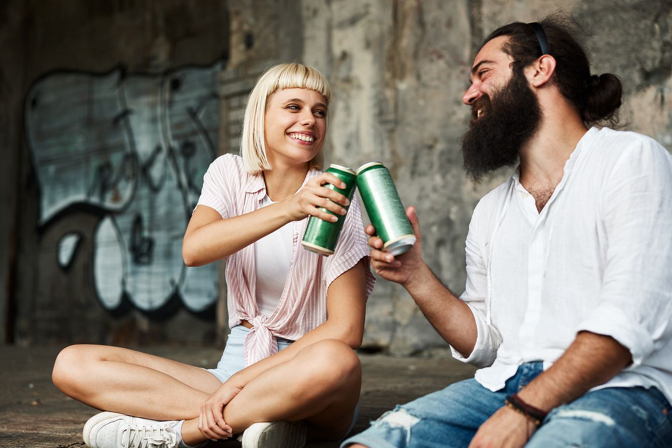 Eine Frau und ein Bier sitzen auf einer Mauer und stoßen mit Bier an
