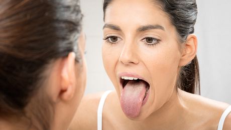 Eine Frau inspiziert ihre Zunge im Spiegel - Foto: iStock/4FR