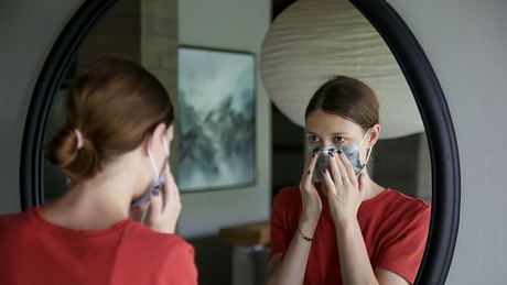 Frau mit Maske schaut in den Spiegel - Foto: iStock / triocean