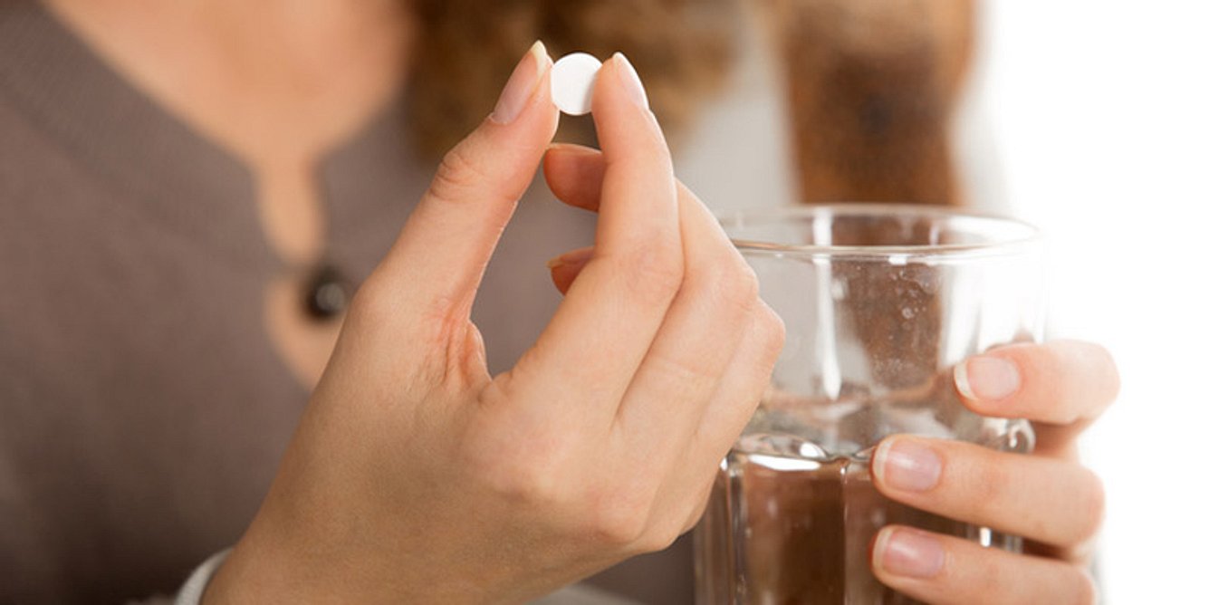 Eine Frau hält ein Medikament und ein Glas Wasser in der Hand
