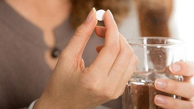 Eine Frau hält ein Medikament und ein Glas Wasser in der Hand - Foto: iStock