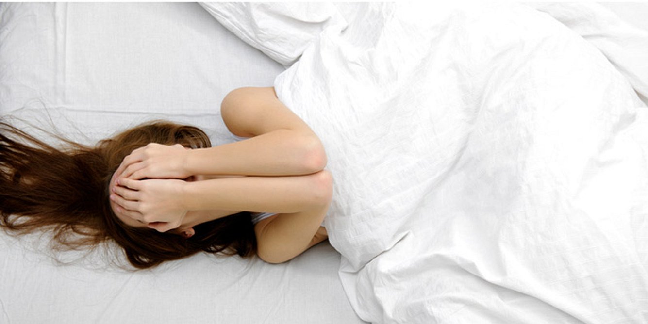 Eine Frau liegt im Bett und hält sich die Hände vor das Gesicht