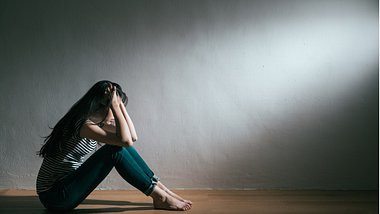 Eine junge Frau sitzt verzweifelt auf dem Boden - Foto: istock_PRImageFactory