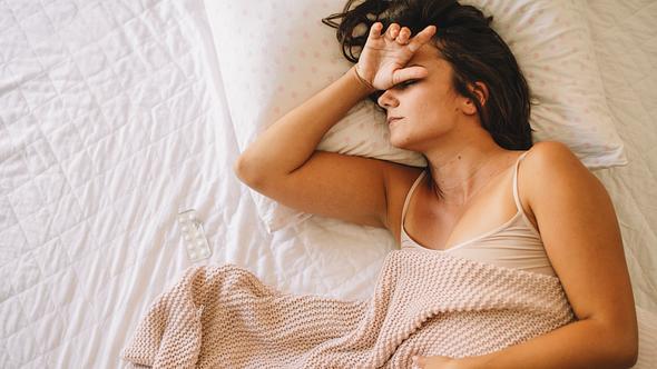 Frau mit PMS liegt im Bett - Foto: iStock/Boris Jovanovic