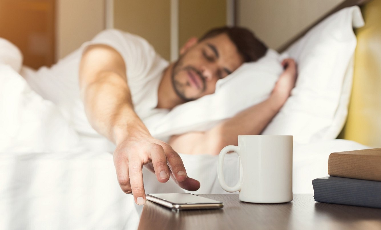 Mann greift im Bett nach seinem Handy
