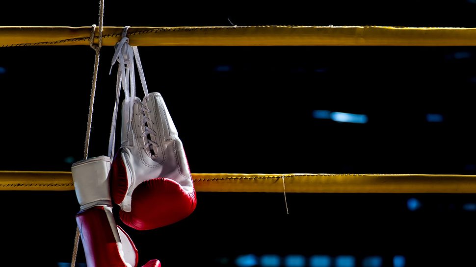 Boxhandschuhe hängen am Boxring - Foto: Istock/PongsakornJun