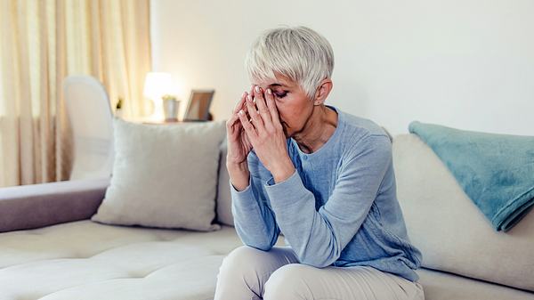 Eine Frau sitzt auf dem Sofa und stützt den Kopf in die Hände - Foto: iStock/Jelena Stanojkovic