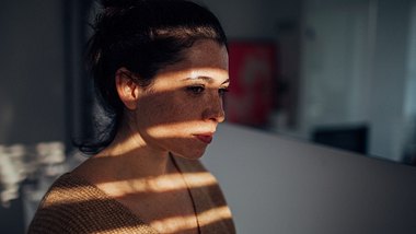 Eine Frau sitzt im Dunkeln und schaut aus dem Fenster - Foto: iStock_AleksandarNakic