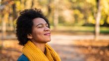 Eine Frau lächelt mir geschlossenen Augen in einem herbstlichen Park. - Foto: iStock/DjelicS
