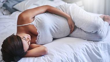 Schwangere Frau liegt seitlich auf dem Bett und schläft - Foto: iStock/peopleimages