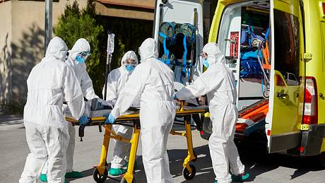Sanitäter in Schutzkleidung schieben Trage in Krankenwagen - Foto: iStock/Morsa Images