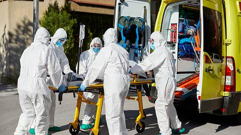 Sanitäter in Schutzkleidung schieben Trage in Krankenwagen - Foto: iStock/Morsa Images