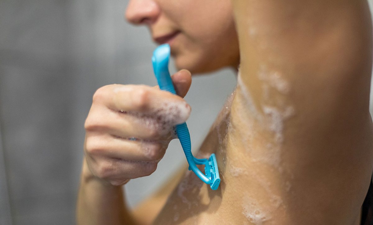 Eine Frau rasiert sich die Achsel unter der Dusche