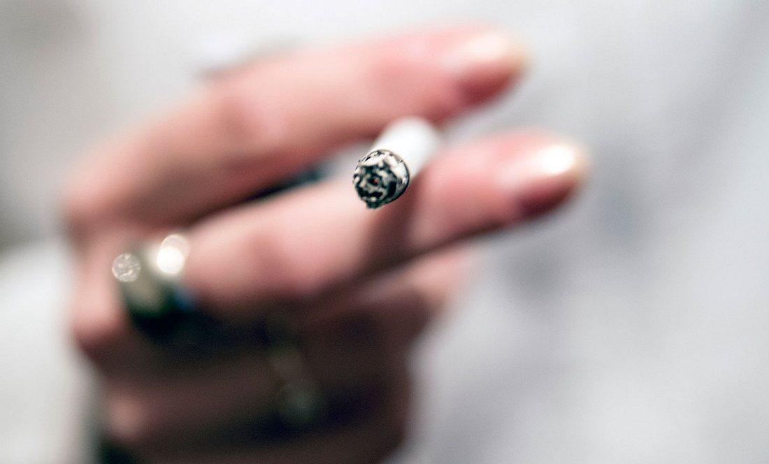 Weibliche Hand hält eine brennende Zigarette