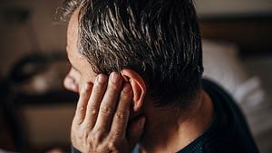 Ein Mann hält sich sein linkes Ohr zu - Foto: iStock_Nes