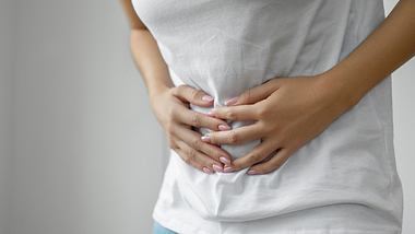 Frau hält sich den schmerzenden Bauch - Foto: iStock/bymuratdeniz