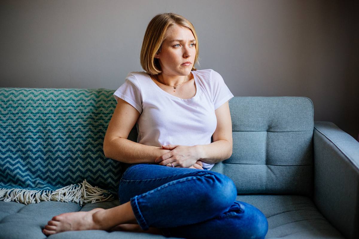 Frau mit Bauchschmerzen sitzt auf dem Sofa und hält sich den Bauch