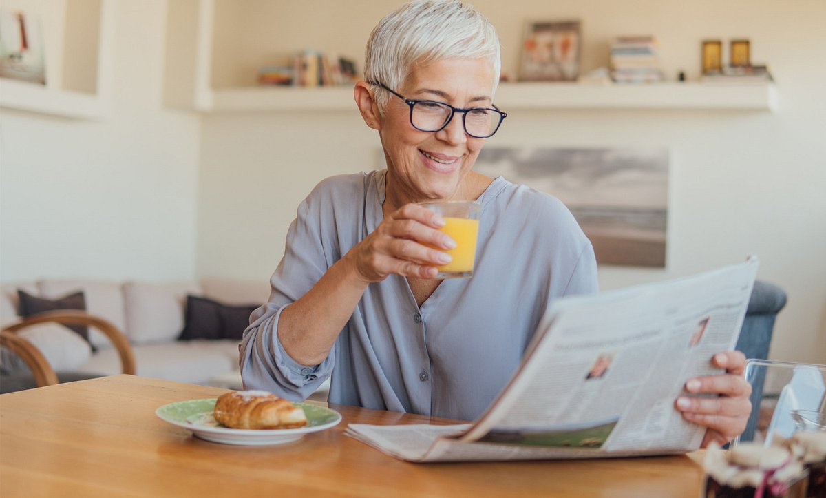Frau liest Zeitung mit Glas in der Hand
