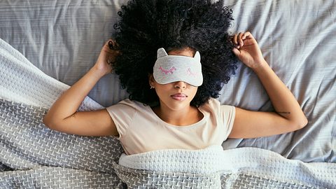 Eine Frau liegt unter einer Decke in einem Bett. - Foto: iStock/LaylaBird