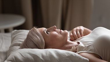 Eine Frau liegt mit geöffneten Augen im Bett - Foto: iStock_fizkes