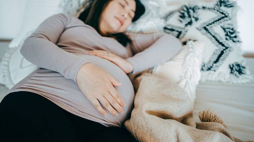 Eine Schwangere liegt im Bett und schläft - Foto: iStock/AsiaVision