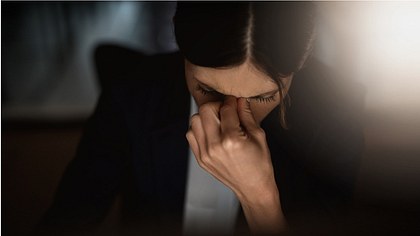 Eine Frau fasst sich mit gesenktem Kopf an den Nasenrücken - Foto: istock_PeopleImages