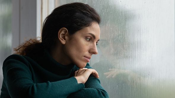 Frau guckt traurig aus dem Fenster - Foto: iStock/fizkes